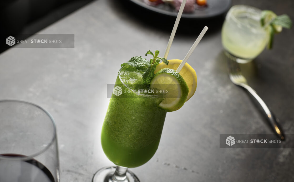 Bright green cocktail garnished with fresh mint lemon and lime on a restaurant table