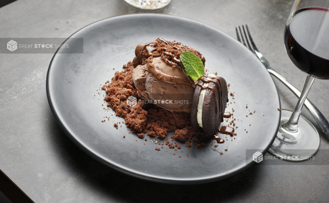 A chocolate ice cream dessert with fresh mint and an icing filled chocolate cookie at a restaurant table