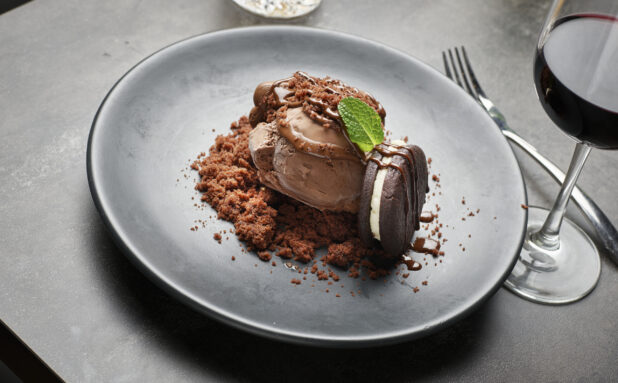 A chocolate ice cream dessert with fresh mint and an icing filled chocolate cookie at a restaurant table