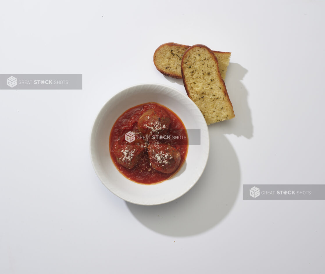 Meatballs in tomato sauce in a white bowl with garlic bread on a white background