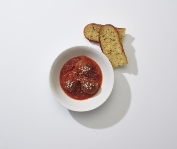 Meatballs in tomato sauce in a white bowl with garlic bread on a white background