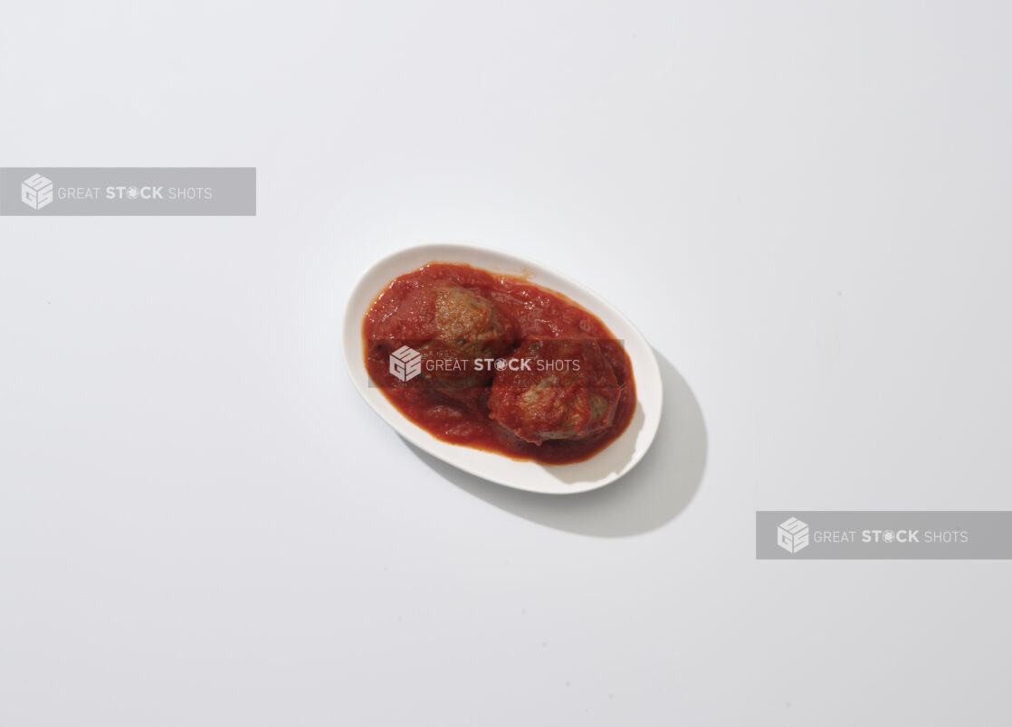 Two Italian meatballs in tomato sauce on a white plate on a white background