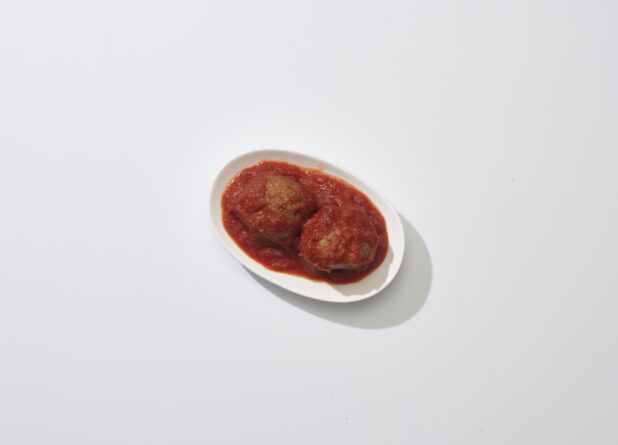 Two Italian meatballs in tomato sauce on a white plate on a white background