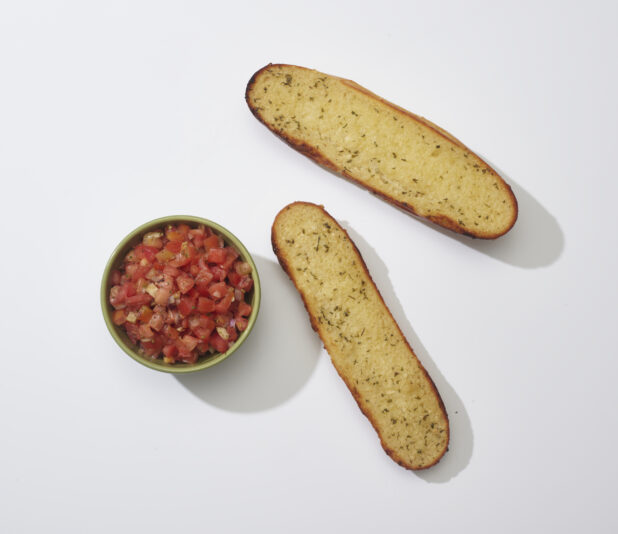 Garlic bread with a bowl of Bruschetta topping on a white background