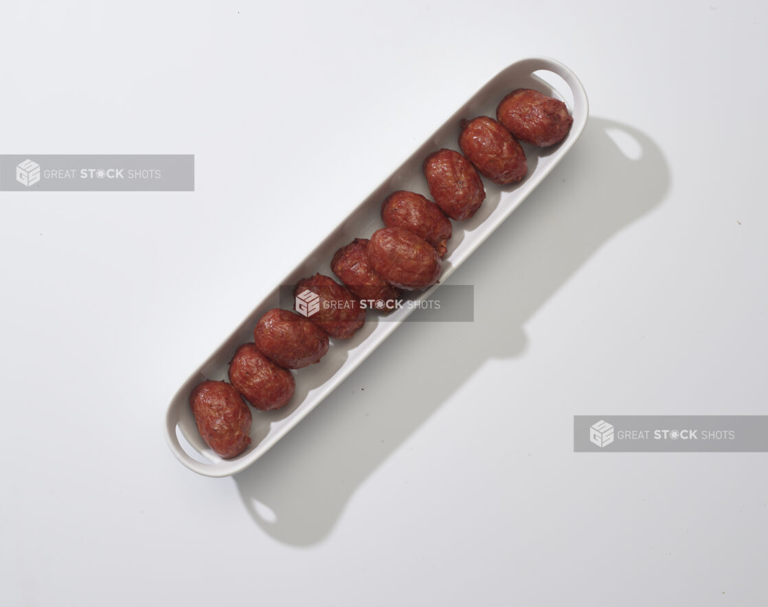 A narrow white platter of meatballs on a white background