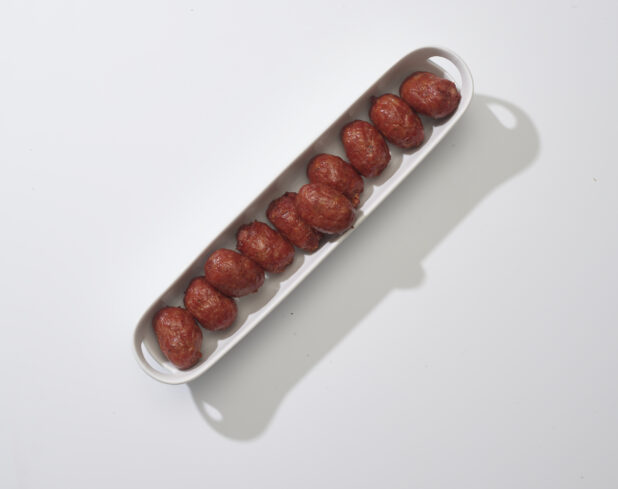 A narrow white platter of meatballs on a white background