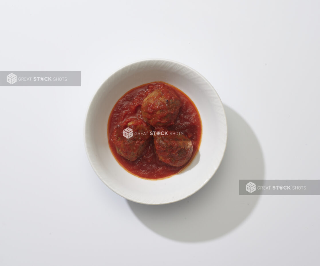 A bowl with three meatballs in tomato sauce on a white background