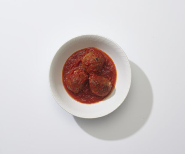 A bowl with three meatballs in tomato sauce on a white background