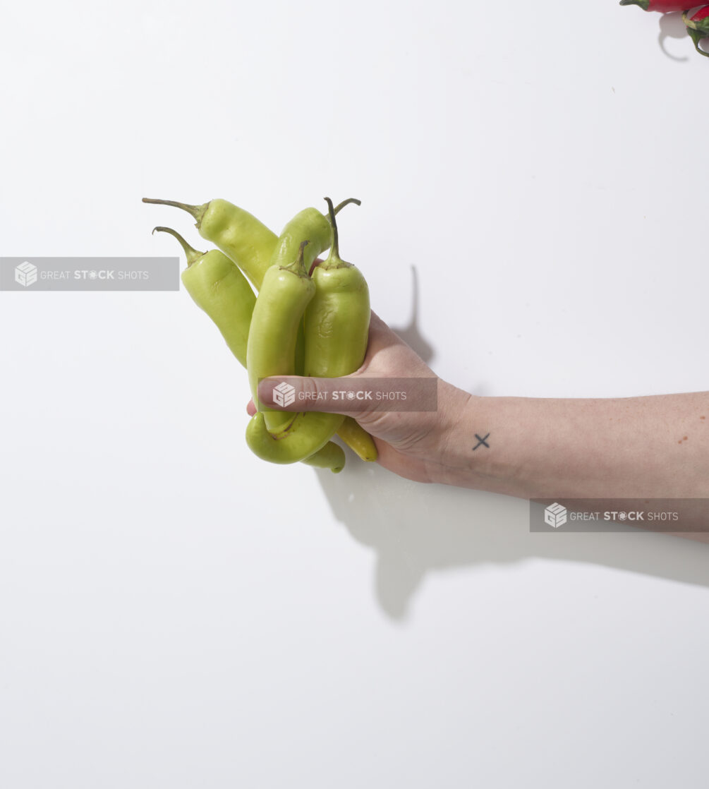 Hand holding banana peppers on a white background