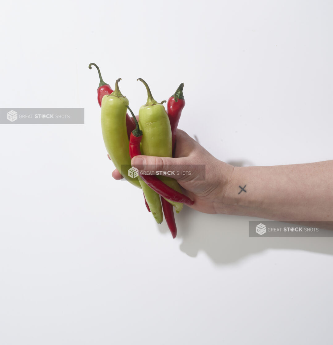 Hand holding fresh green and red chili peppers on a white background