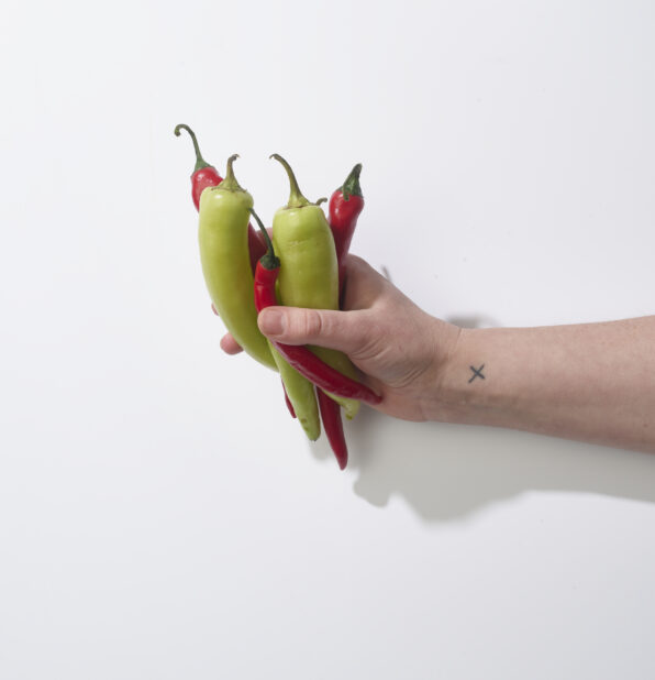 Hand holding fresh green and red chili peppers on a white background