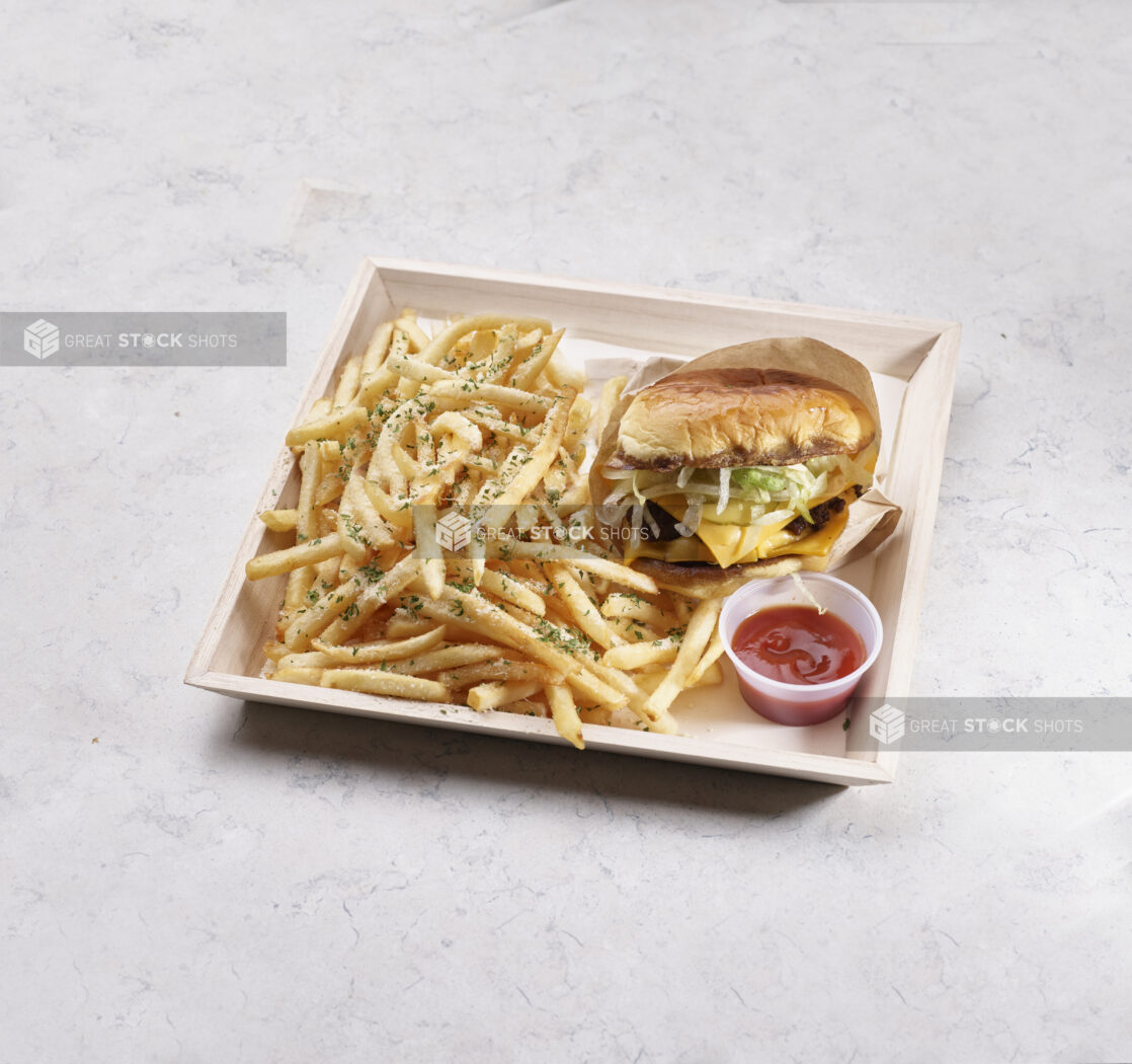 Cheeseburger with herb french fries on a wooden catering tray with a plastic ramekin of ketchup