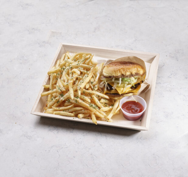 Cheeseburger with herb french fries on a wooden catering tray with a plastic ramekin of ketchup