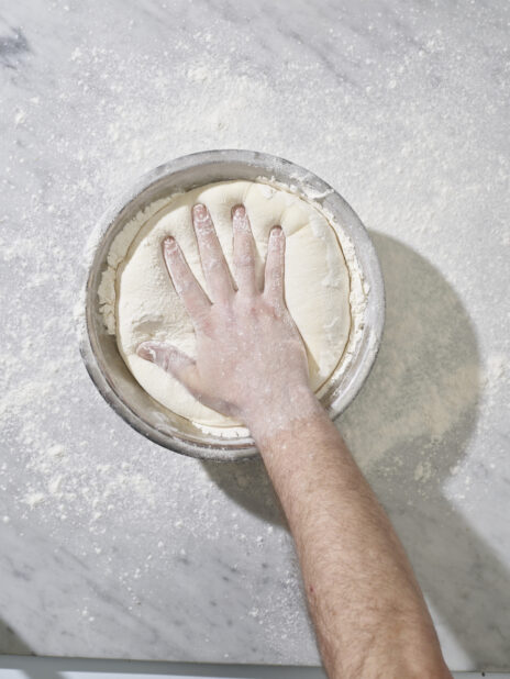 A hand pressing down into a bowl of raw dough