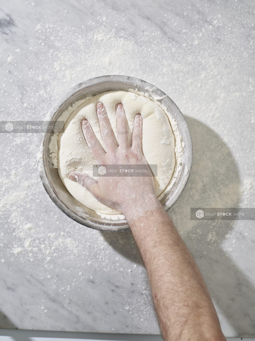 A hand pressing down into a bowl of raw dough