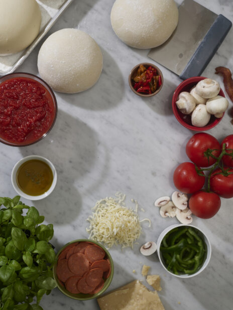An overhead view of pizza dough and pizza ingredients on a marble background