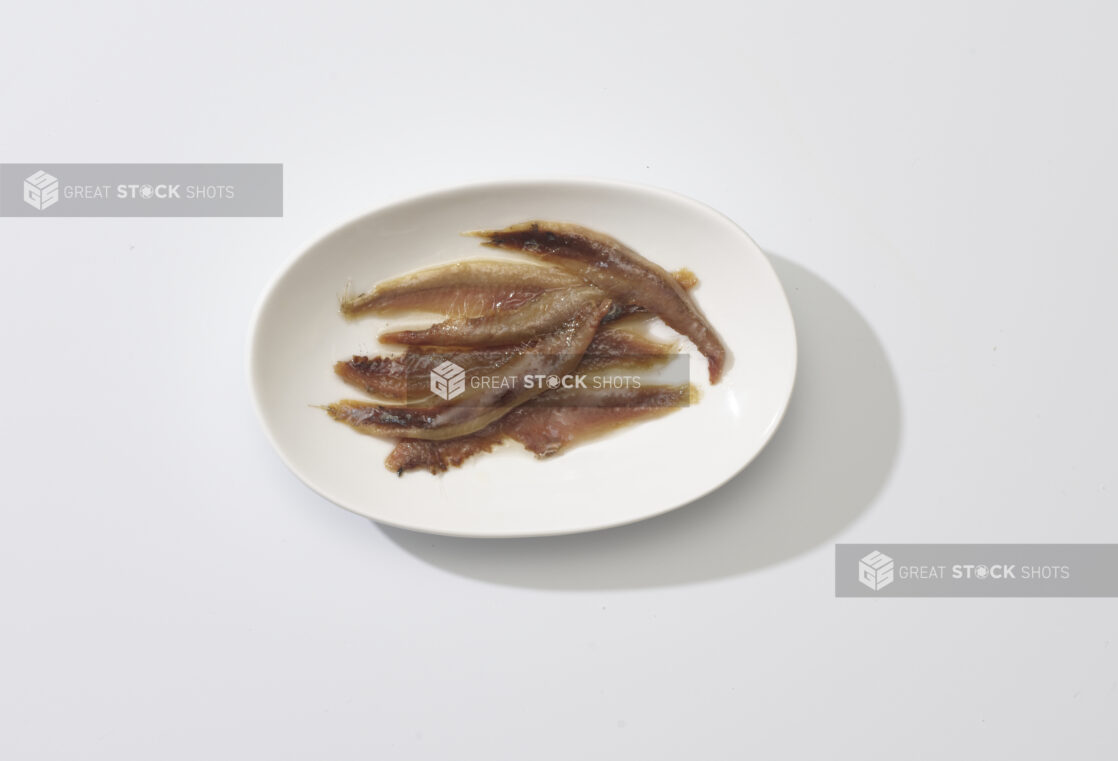 A white plate of anchovies on a white background