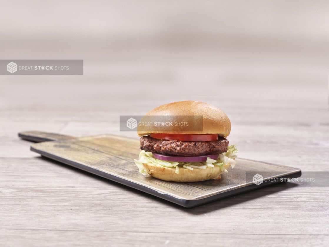 Hamburger with lettuce, tomato and red onion on a wooden board on a wooden background