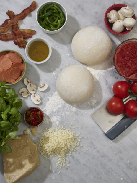 And overhead view of pizza ingredients and pizza dough on a white background