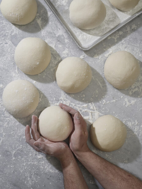 A baker's hands shaping balls of raw pizza dough on a marble surface