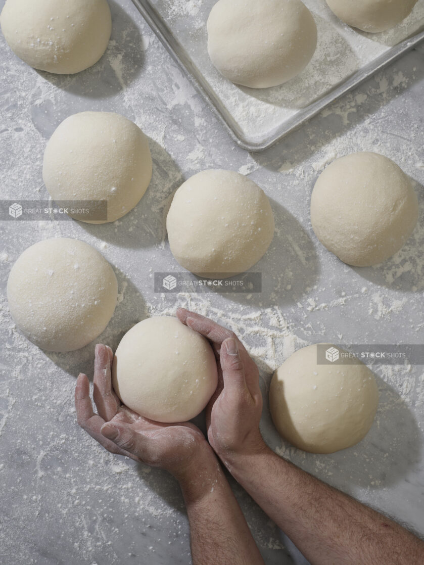 A baker's hands shaping balls of raw pizza dough on a marble surface