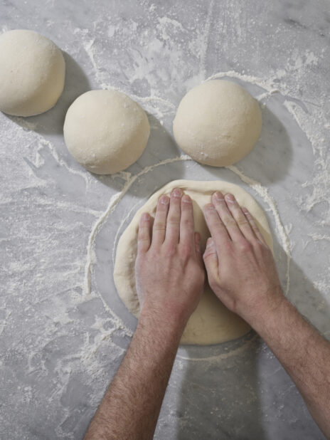 Pizza chef shaping raw pizza dough on a marble prep service dusted with flour