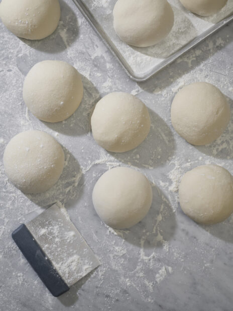 An overhead view of balls of pizza dough on a marble prep surface