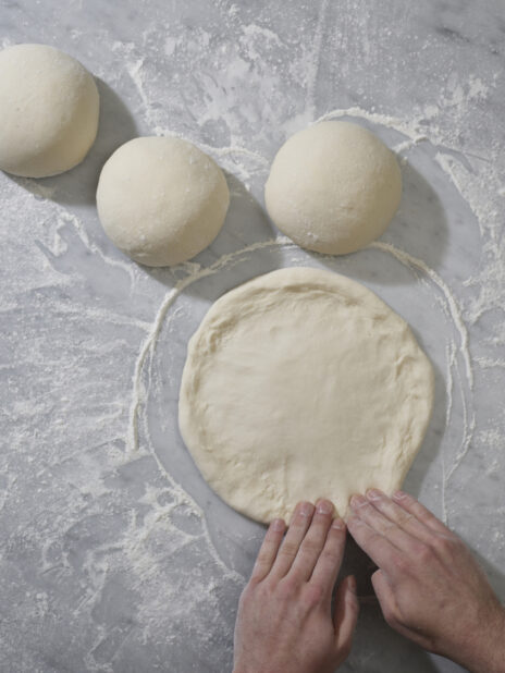 Pizza chef shaping pizza dough on a marble background dusted with flour
