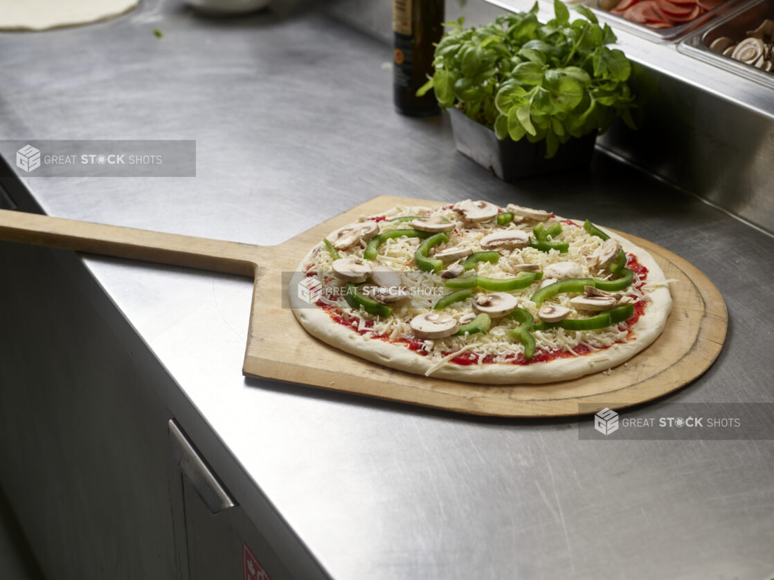 An uncooked small veggie pizza on a pizza peel at a Prep Station