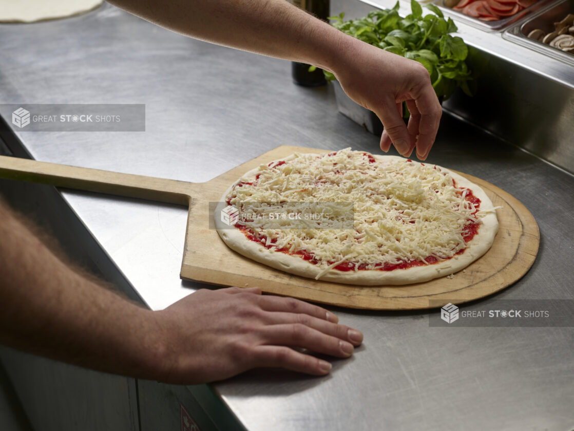 A cook preparing a small pizza on a pizza peel in a commercial kitchen