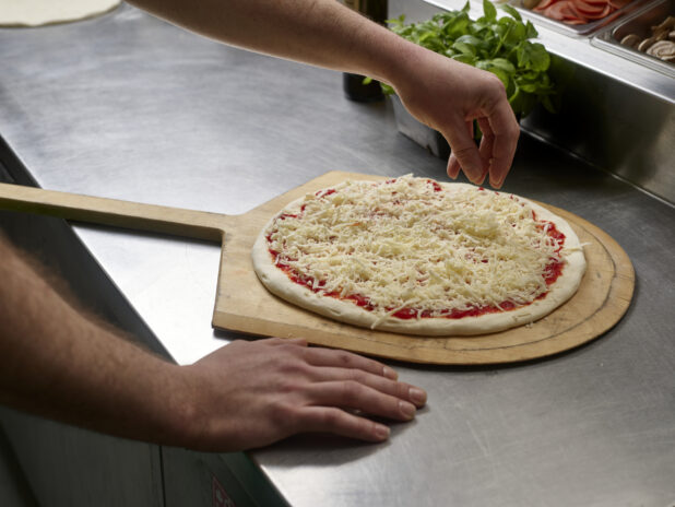 A cook preparing a small pizza on a pizza peel in a commercial kitchen