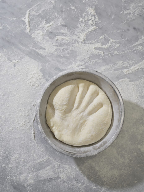 An overhead view of a handprint in raw pizza dough in a bowl on a marble surface