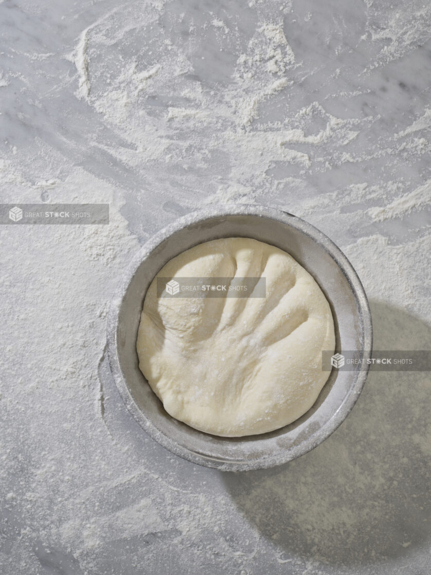 An overhead view of a handprint in raw pizza dough in a bowl on a marble surface