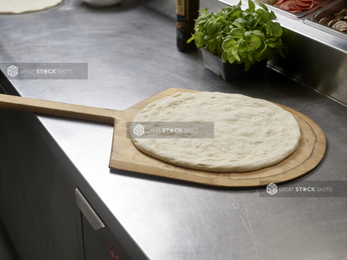 Shaped pizza dough ready for toppings on a pizza peel in a commercial kitchen