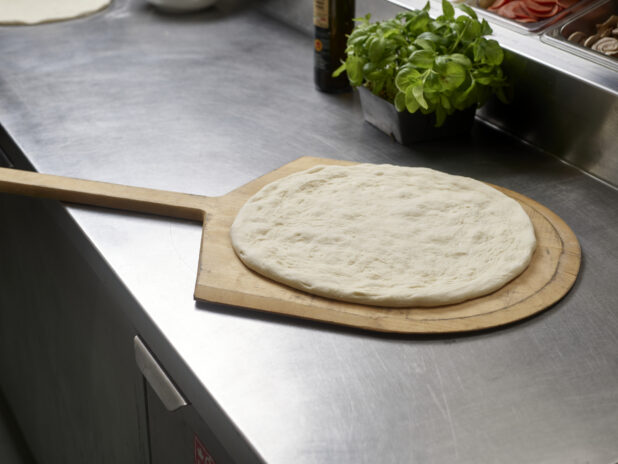 Shaped pizza dough ready for toppings on a pizza peel in a commercial kitchen