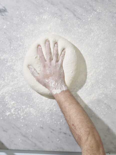 A hand pressing down into floury dough on a marble work surface