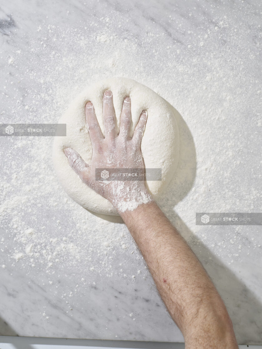 A hand pressing down into floury dough on a marble work surface