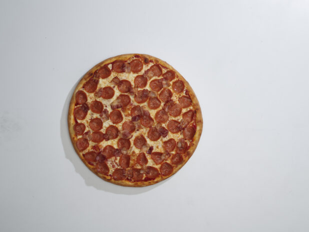 Whole traditional unsliced pepperoni pizza on a white background