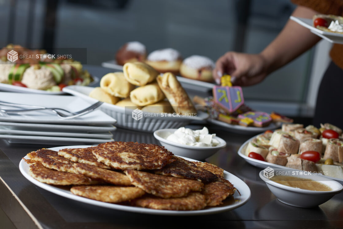 A person picking up a dreidel cookie from a buffet of Hanukkah food