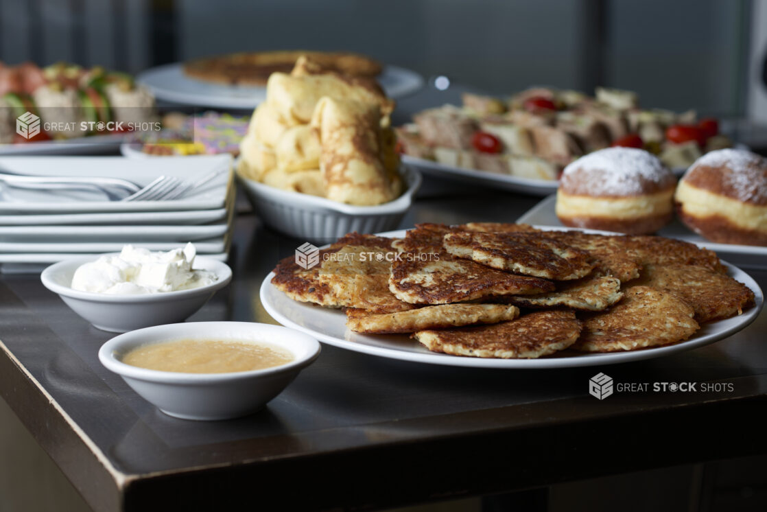 A buffet of assorted plates of Hanukkah food, latkes in foreground