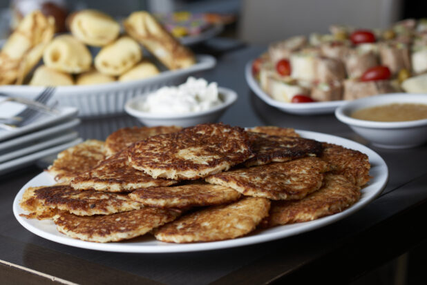 A plate of potato latkes on a buffet table of assorted dishes, close-up
