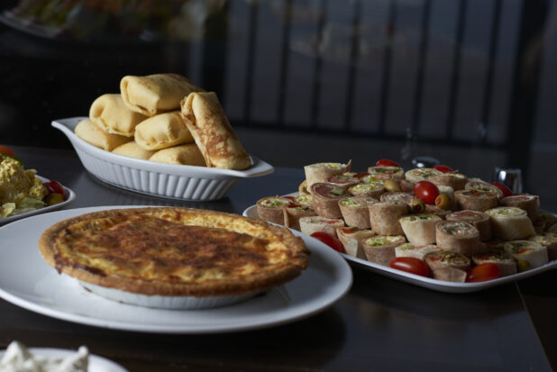 A buffet table with blintzes, cocktail sandwiches a savoury pie on a white plate