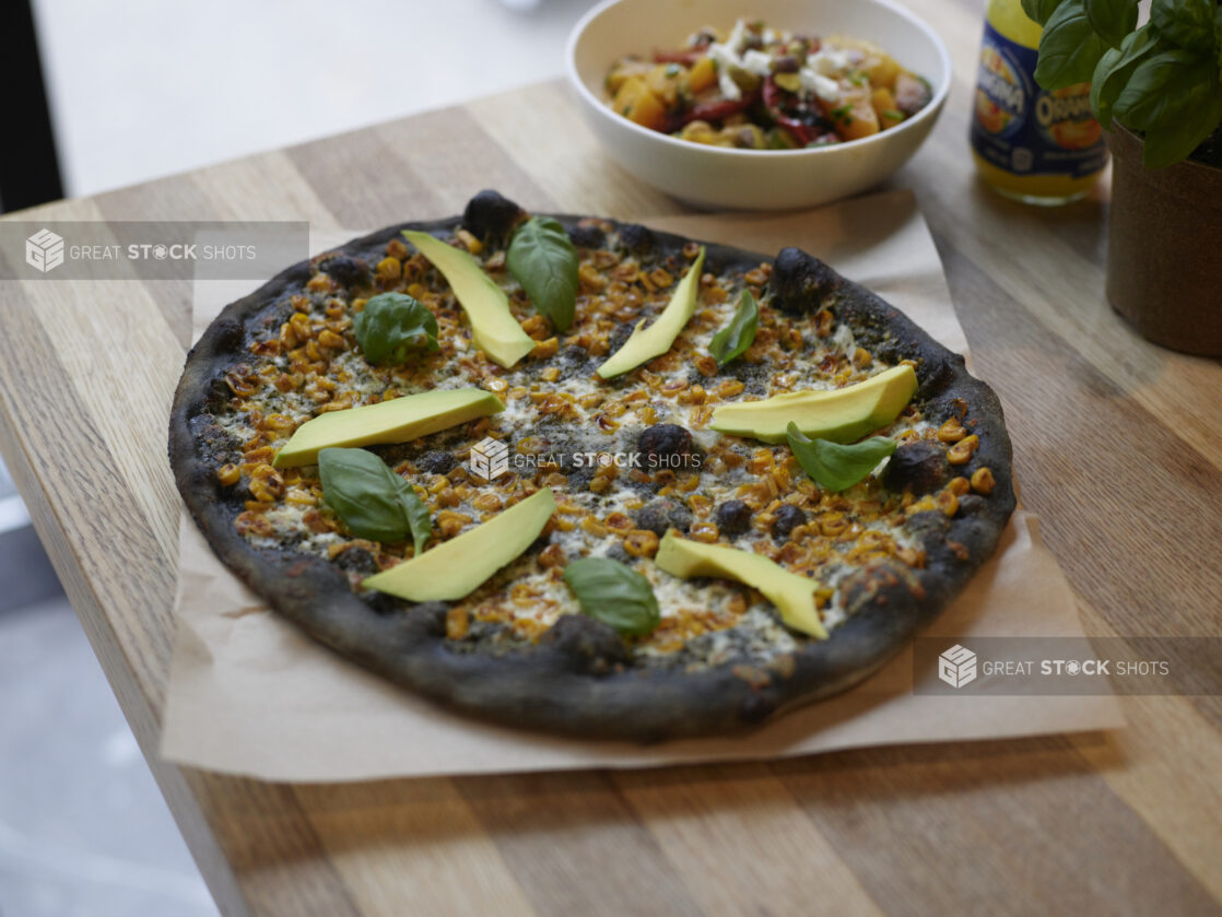 An Ikasumi Pizza with avocado and basil on parchment paper on a wooden table, high angle