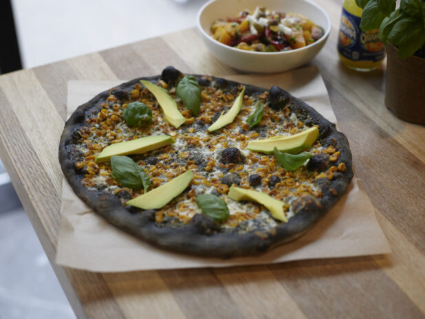 An Ikasumi Pizza with avocado and basil on parchment paper on a wooden table, high angle