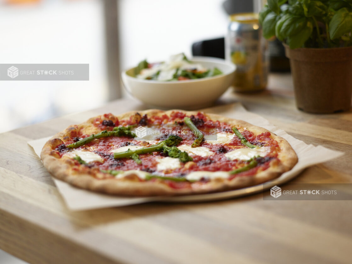 A Neapolitan-style Margherita pizza with rapini on a wooden table with side salad