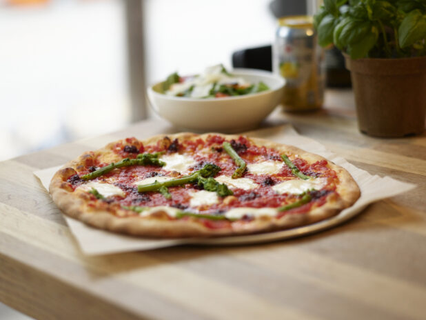 A Neapolitan-style Margherita pizza with rapini on a wooden table with side salad