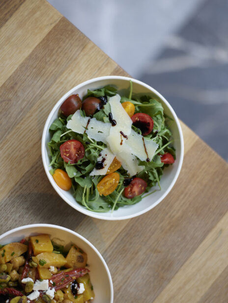 Arugula salad with shaved Parmesan and cherry tomatoes in a white bowl on a wooden table, overhead