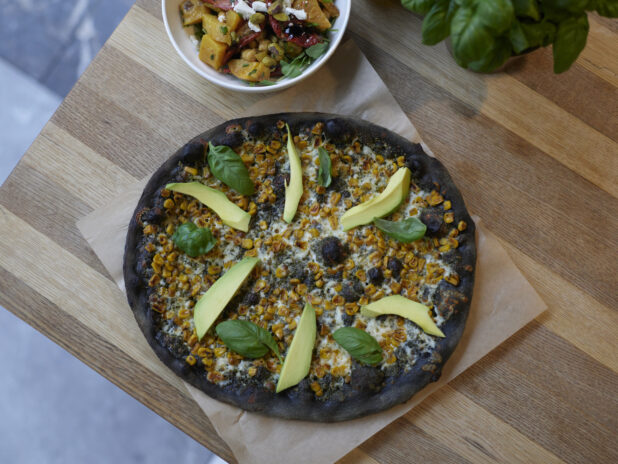 An Ikasumi California style pizza on parchment on a wooden table