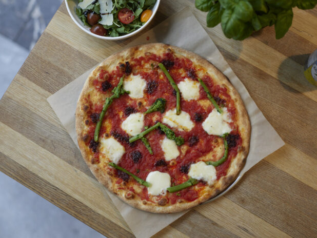 A Neapolitan-style Margherita pizza with rapini on parchment paper on a wooden table