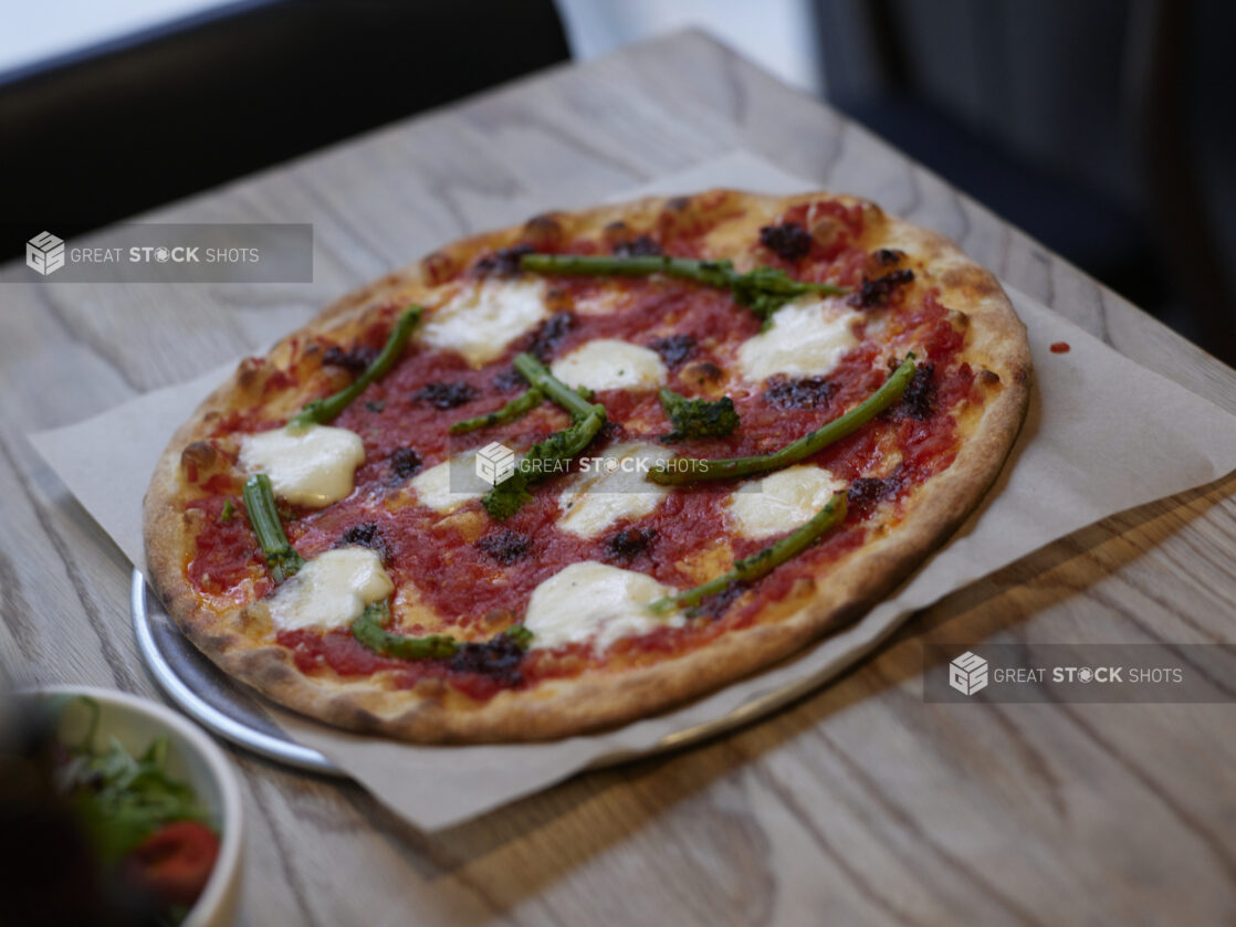 A thin crust Neapolitan-style Margherita Pizza with rapini on parchment paper